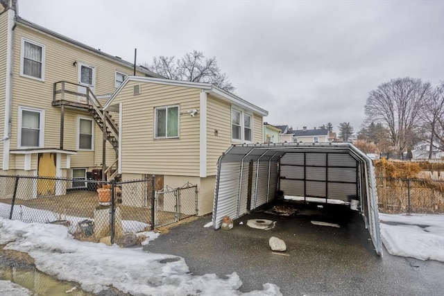 view of snowy exterior with a detached carport, driveway, and fence