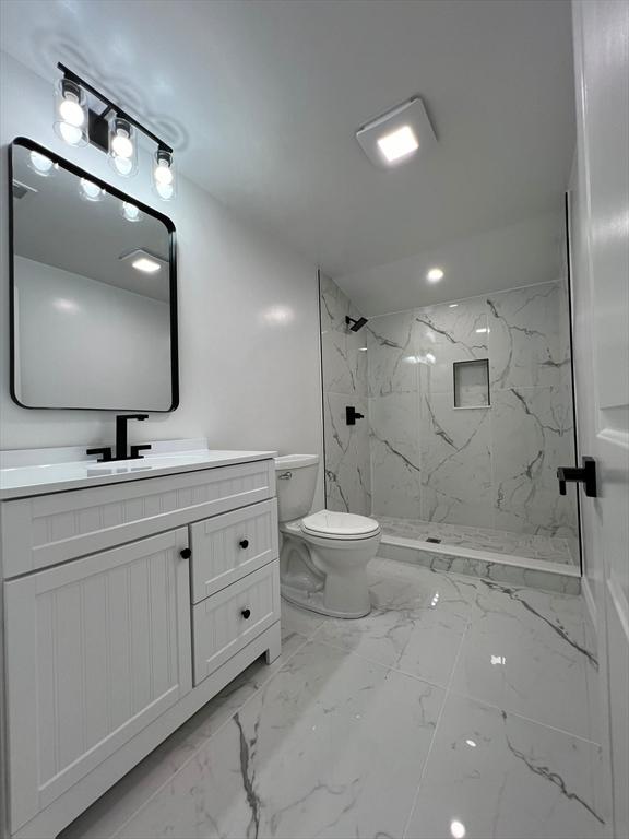 bathroom with tile patterned flooring, toilet, vanity, and a tile shower