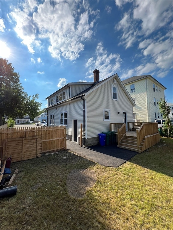 rear view of property featuring a wooden deck and a lawn