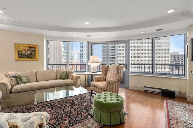 living room with baseboard heating, hardwood / wood-style floors, a raised ceiling, and ornamental molding