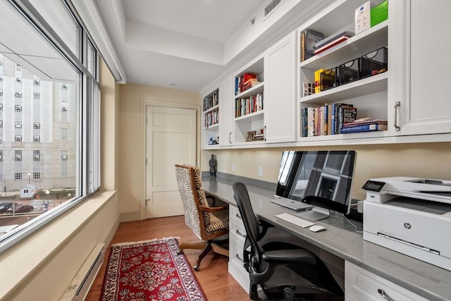 home office with a baseboard heating unit, light hardwood / wood-style flooring, and built in desk