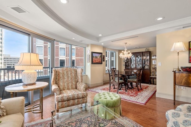 living room with ornamental molding, a raised ceiling, an inviting chandelier, and hardwood / wood-style floors