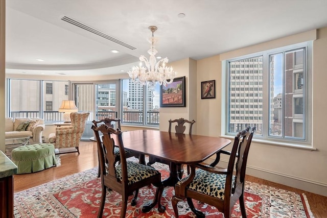 dining area with a notable chandelier, a raised ceiling, and light hardwood / wood-style floors