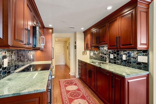 kitchen featuring sink, backsplash, light hardwood / wood-style flooring, and light stone countertops