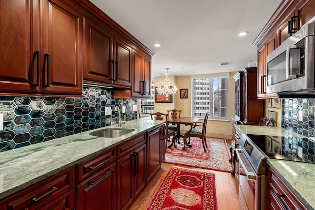 kitchen with light hardwood / wood-style floors, tasteful backsplash, hanging light fixtures, an inviting chandelier, and stainless steel appliances