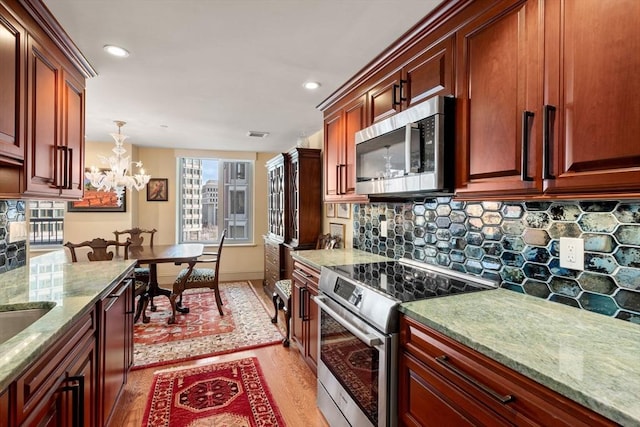 kitchen with pendant lighting, appliances with stainless steel finishes, an inviting chandelier, decorative backsplash, and light stone counters