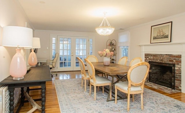 dining room featuring a brick fireplace, french doors, an inviting chandelier, and ornamental molding