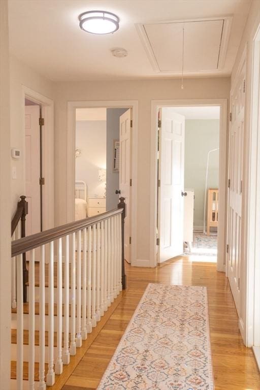 hallway with attic access, light wood-style flooring, and baseboards