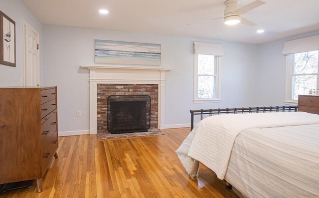 bedroom with a brick fireplace, baseboards, recessed lighting, light wood-style flooring, and a ceiling fan