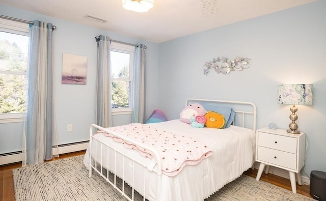 bedroom with visible vents, wood finished floors, and a baseboard heating unit