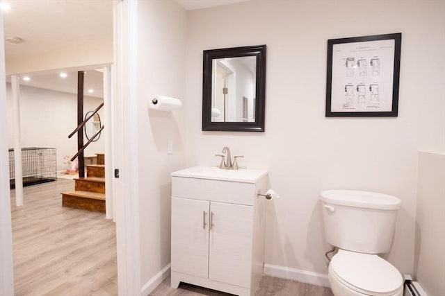 bathroom featuring toilet, a baseboard heating unit, wood finished floors, baseboards, and vanity