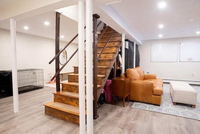 finished below grade area featuring recessed lighting, a baseboard heating unit, wood finished floors, and stairway