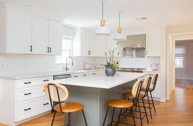 kitchen with a kitchen bar, range hood, white cabinets, and visible vents