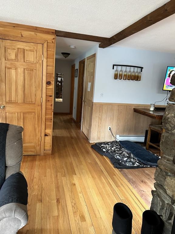 554 Main St, Becket, MA 01223 - living area with wainscoting, light wood-style flooring, beam ceiling, wood walls, and a textured ceiling