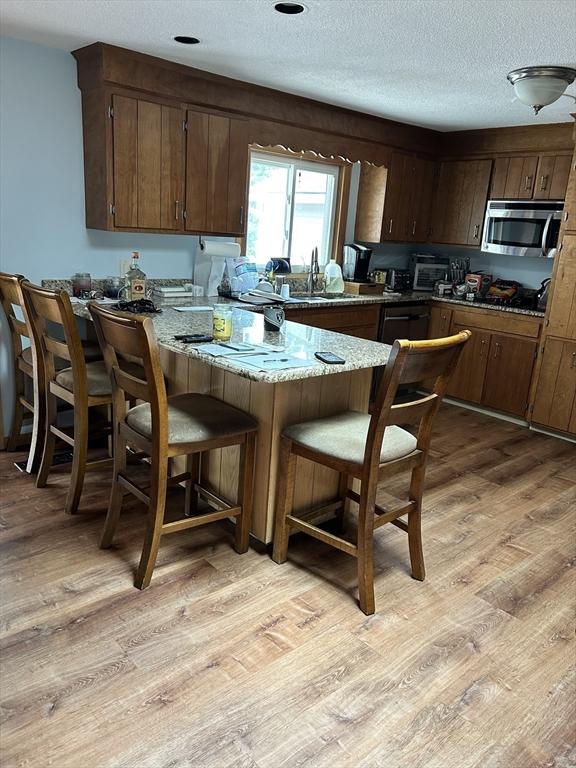 554 Main St, Becket, MA 01223 - kitchen with stainless steel microwave, light wood-style flooring, a sink, a breakfast bar area, and a textured ceiling