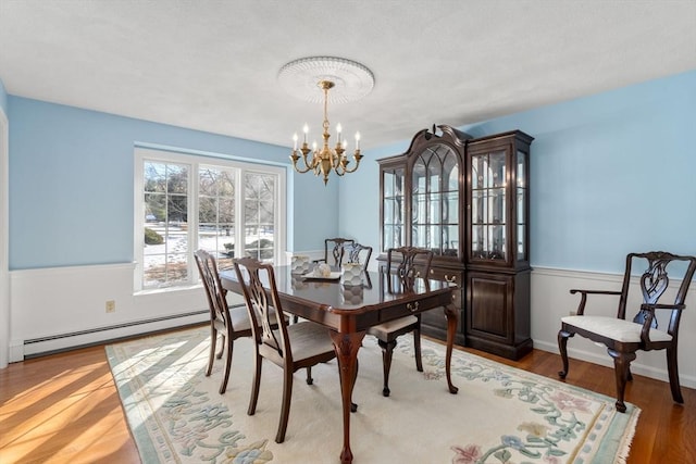 dining area featuring an inviting chandelier, baseboard heating, and wood finished floors