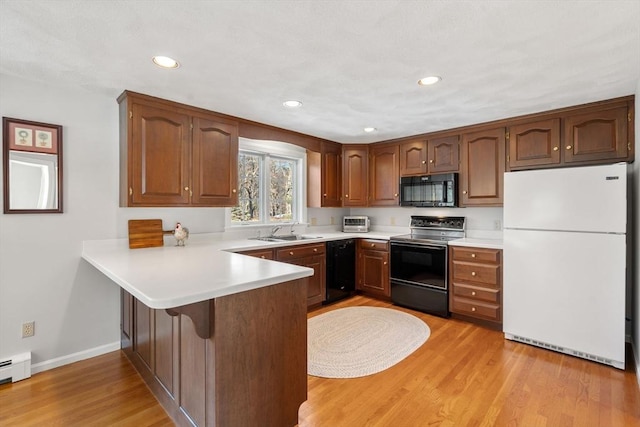 kitchen featuring light countertops, light wood-style flooring, a sink, a peninsula, and black appliances