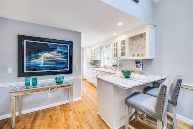 1441 Old Post Rd, Barnstable, MA 02648 - kitchen featuring a breakfast bar area, white cabinetry, glass insert cabinets, light wood-type flooring, and decorative backsplash