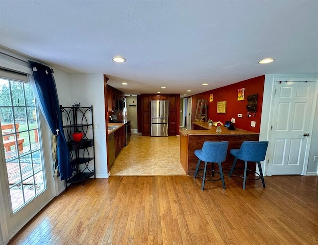 kitchen featuring a kitchen breakfast bar, light wood-style floors, freestanding refrigerator, recessed lighting, and a peninsula