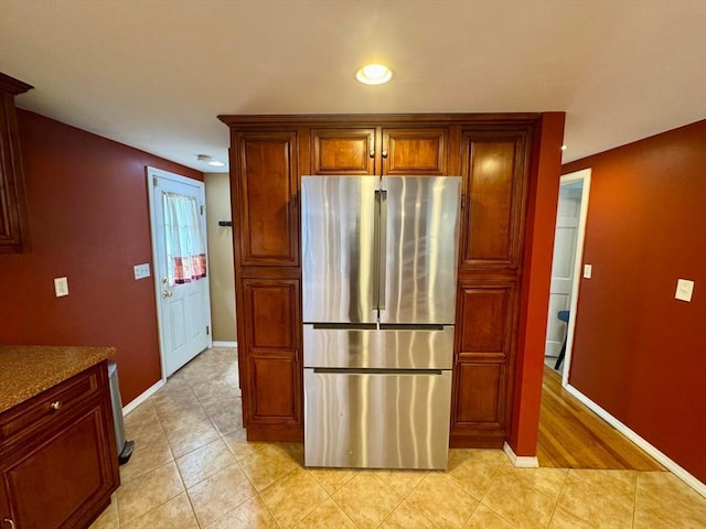kitchen with brown cabinets, freestanding refrigerator, baseboards, light tile patterned flooring, and recessed lighting