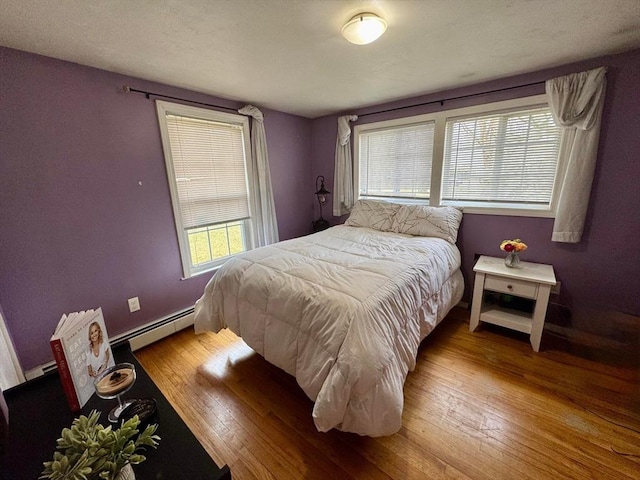 bedroom with a baseboard radiator, hardwood / wood-style floors, and baseboards