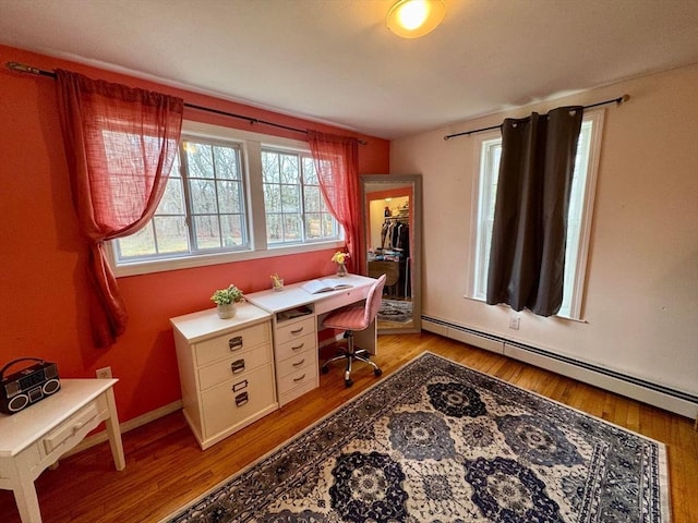 office featuring a baseboard heating unit, light wood-style floors, and a healthy amount of sunlight