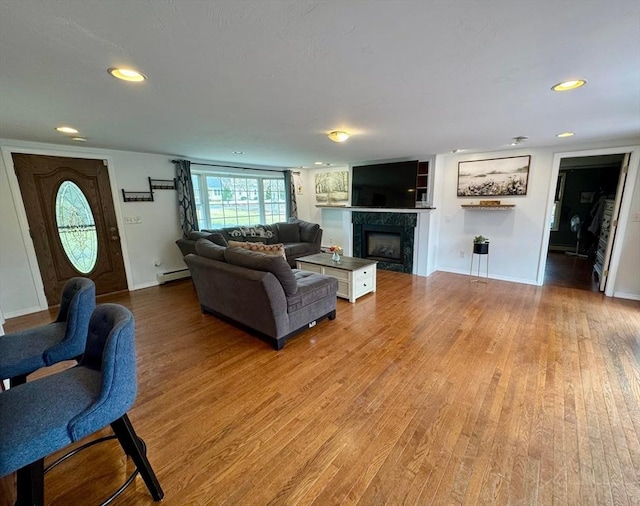 living area featuring recessed lighting, light wood-style flooring, a baseboard heating unit, a fireplace, and baseboards