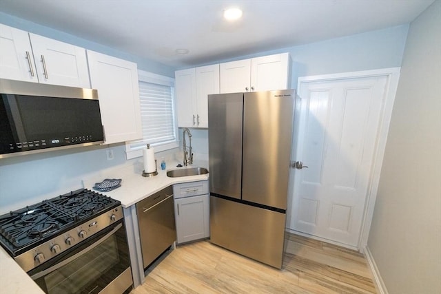 kitchen featuring white cabinets, appliances with stainless steel finishes, sink, and light wood-type flooring