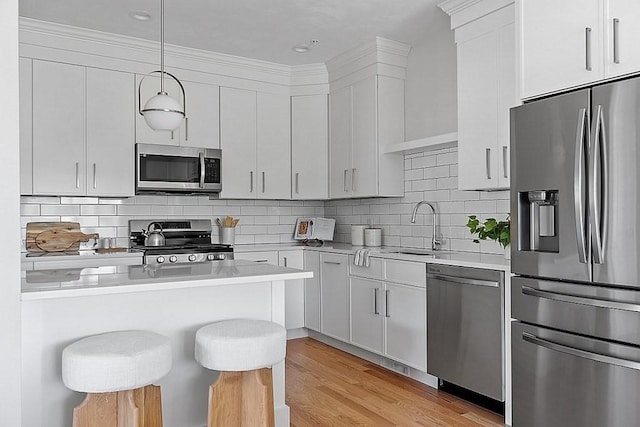 kitchen featuring white cabinets, sink, hanging light fixtures, a kitchen bar, and stainless steel appliances