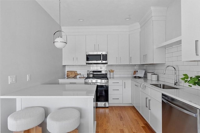 kitchen featuring hanging light fixtures, white cabinetry, stainless steel appliances, and a breakfast bar area