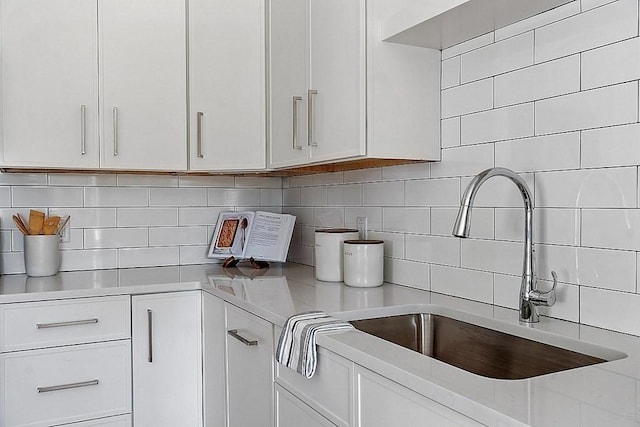 kitchen featuring light stone countertops, backsplash, white cabinetry, and sink