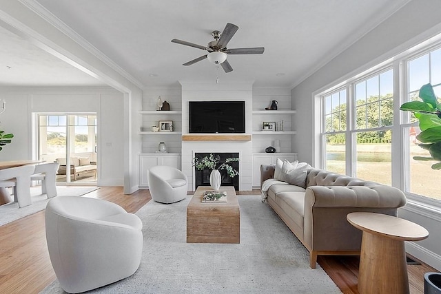 living room featuring ceiling fan, a large fireplace, built in features, and a wealth of natural light