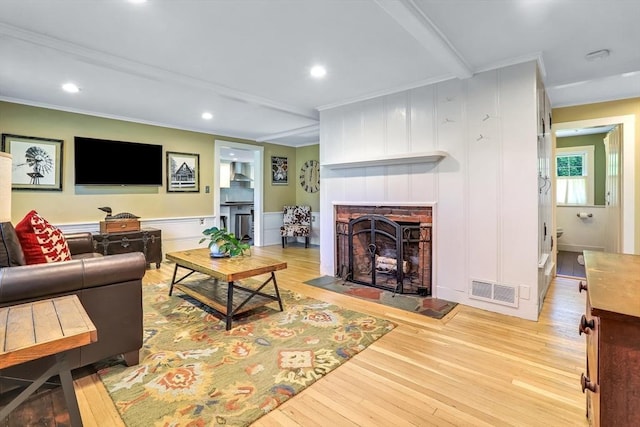 living room featuring wood-type flooring, a decorative wall, a fireplace, crown molding, and recessed lighting
