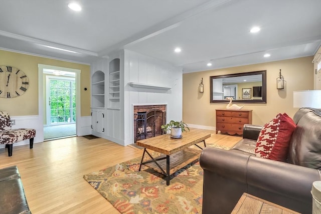 living area featuring wood finished floors, a fireplace with raised hearth, recessed lighting, and built in shelves