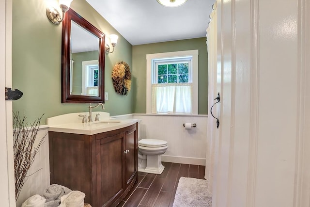 bathroom with wainscoting, wood finish floors, vanity, and toilet