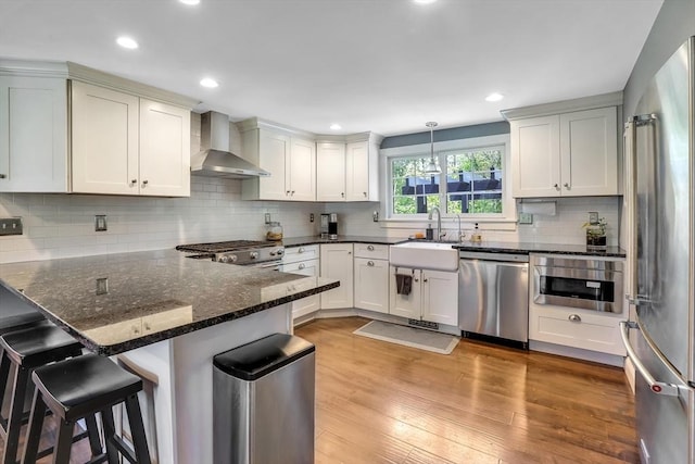 kitchen with appliances with stainless steel finishes, wall chimney exhaust hood, a sink, a peninsula, and decorative backsplash