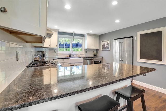 kitchen with a sink, a peninsula, appliances with stainless steel finishes, decorative backsplash, and recessed lighting