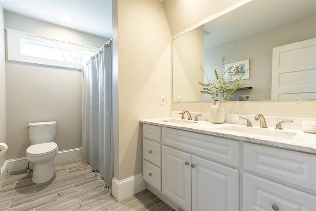 full bath with double vanity, toilet, a sink, and wood finish floors