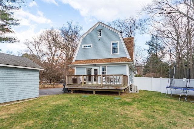 rear view of property with a deck, fence, a gambrel roof, a yard, and a trampoline