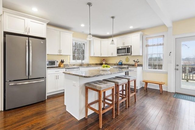 kitchen featuring a kitchen island, white cabinetry, stainless steel appliances, and light stone counters