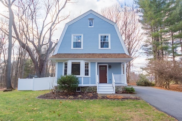 dutch colonial featuring a shingled roof, a front yard, fence, and a gambrel roof