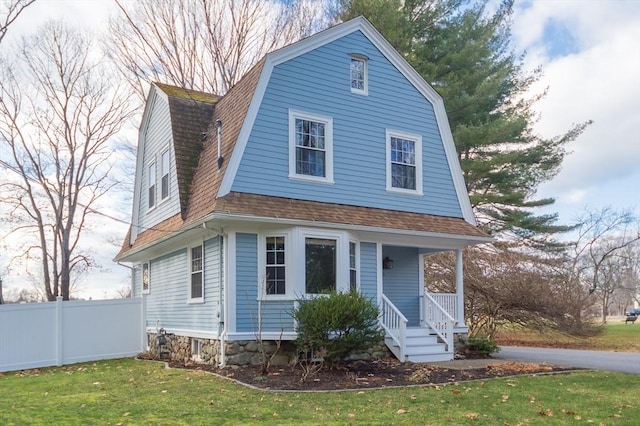 colonial inspired home with a front yard, roof with shingles, fence, and a gambrel roof