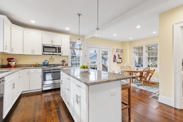 kitchen featuring light stone counters, white cabinets, appliances with stainless steel finishes, a center island, and decorative light fixtures