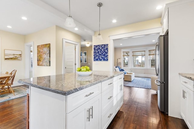 kitchen with light stone counters, a kitchen island, white cabinets, freestanding refrigerator, and decorative light fixtures