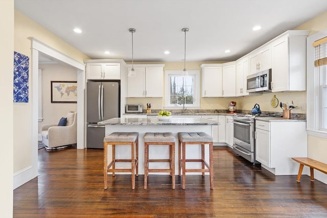 kitchen featuring a center island, light stone countertops, stainless steel appliances, pendant lighting, and a sink