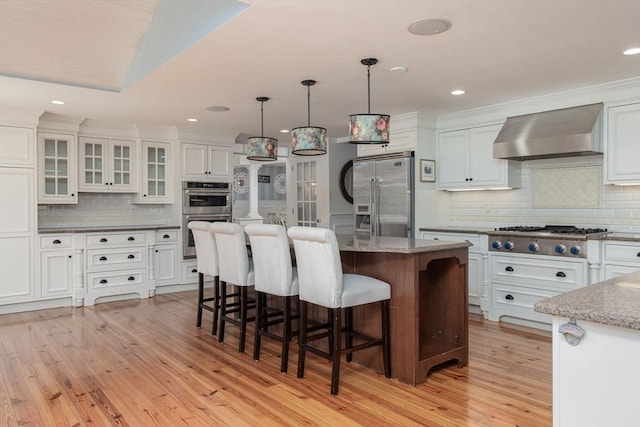 8 Whitaker Ln, Groton, MA 01450 - kitchen with appliances with stainless steel finishes, wall chimney range hood, light wood-type flooring, a breakfast bar area, and backsplash