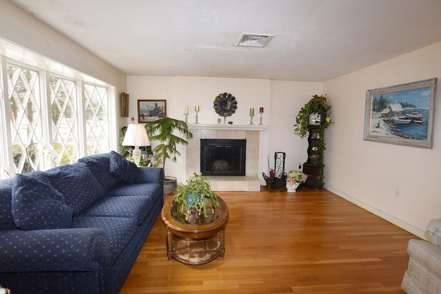 living room featuring a fireplace, wood finished floors, visible vents, and baseboards