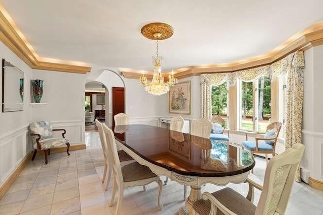 dining area featuring a decorative wall, a wainscoted wall, arched walkways, and a notable chandelier