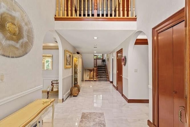 hall featuring arched walkways, marble finish floor, baseboards, and stairway