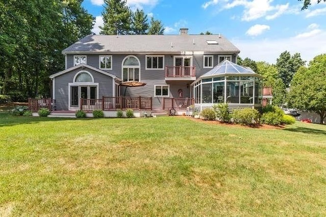 rear view of property with a yard, a wooden deck, a balcony, and a chimney